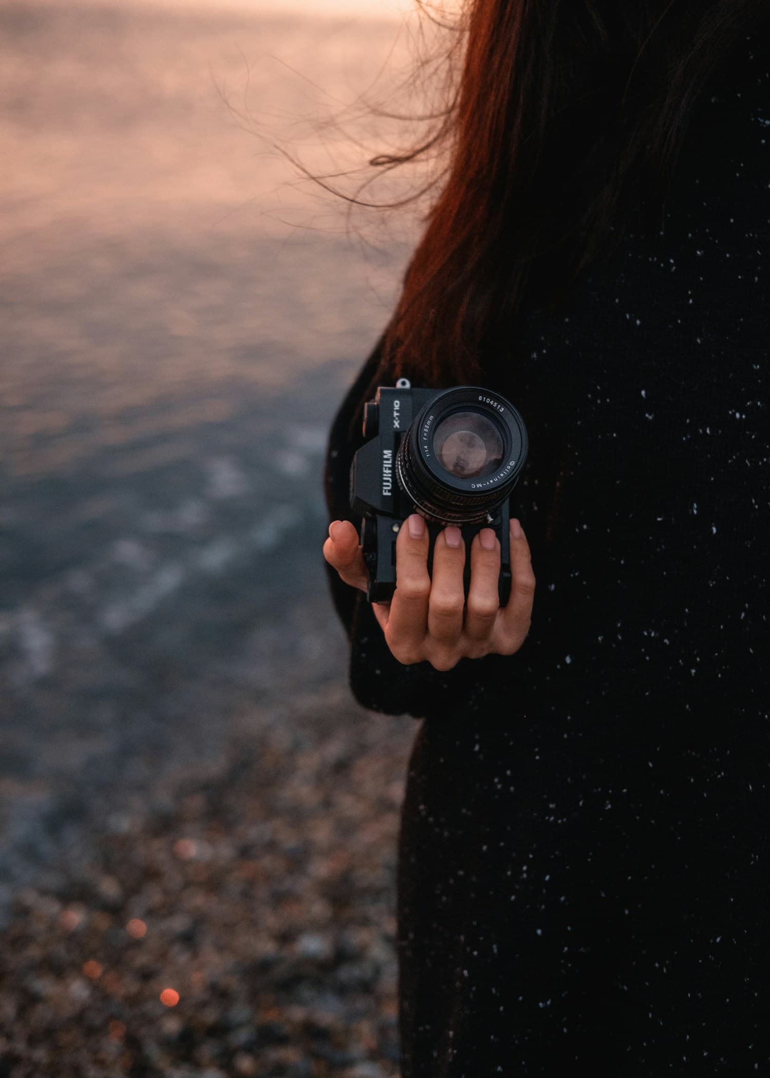 Photographer holding a camera near the ocean at dusk.