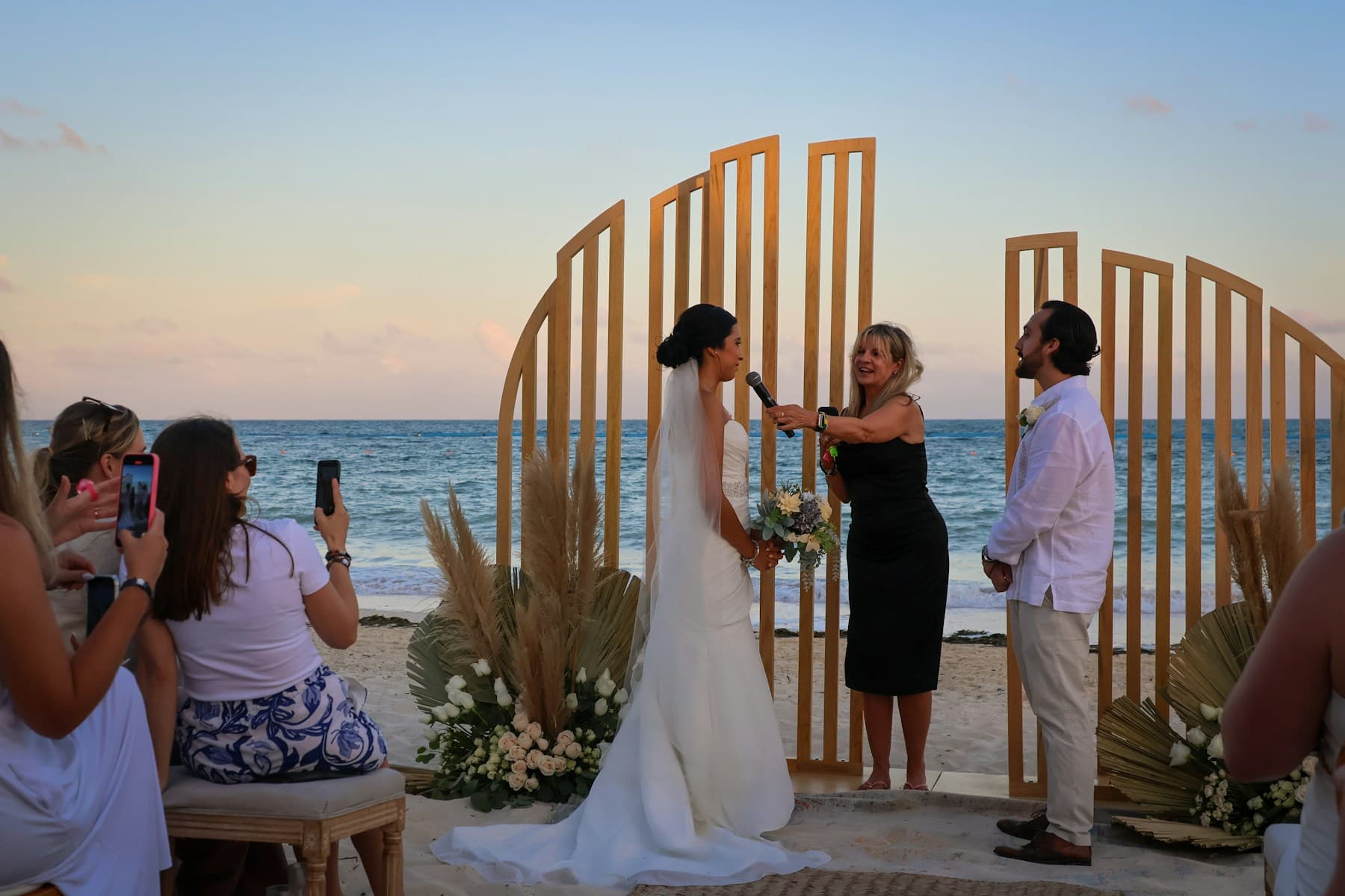 Beach wedding ceremony framed by a modern structure at sunset.