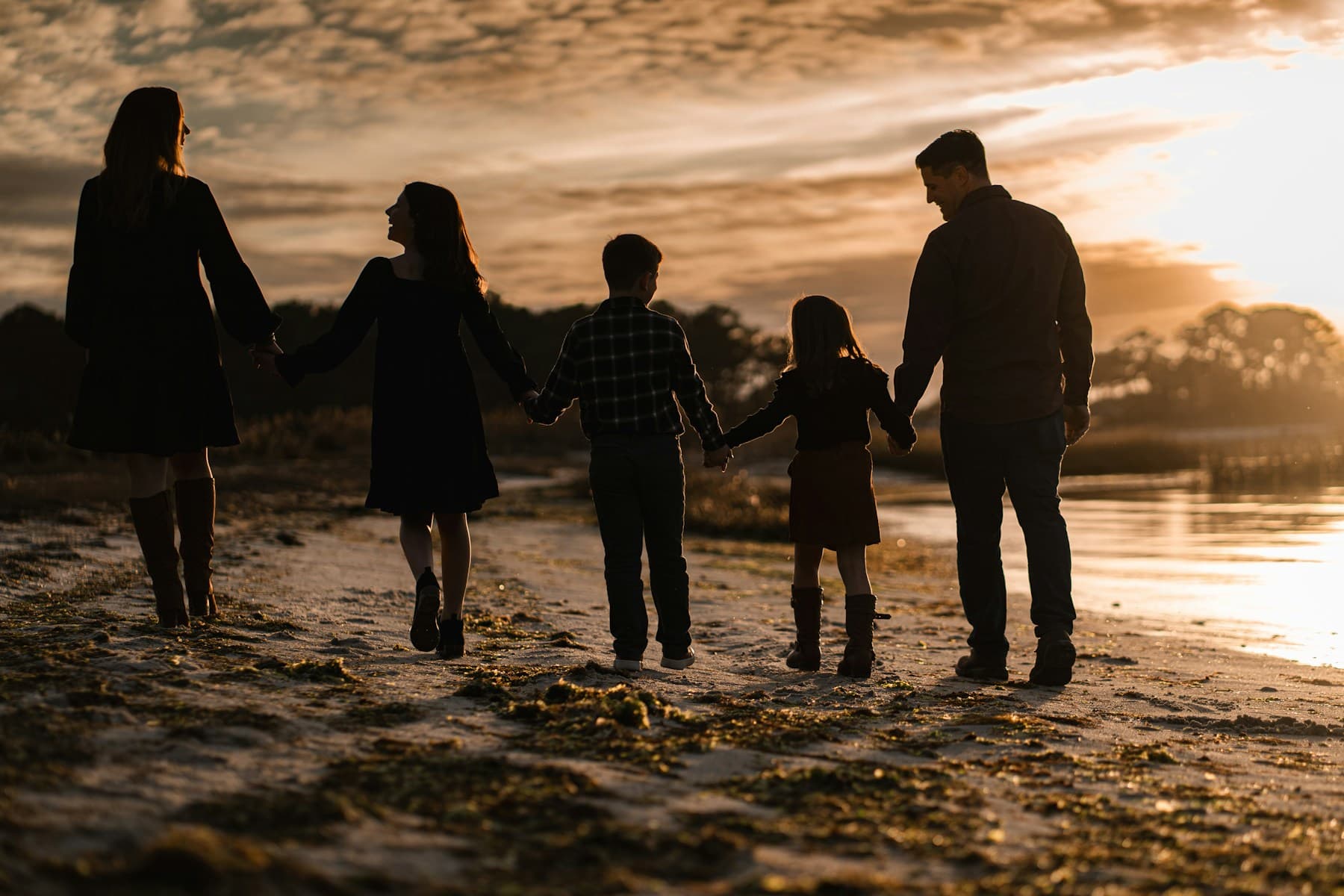 Family of five walking together on the beach at sunset.