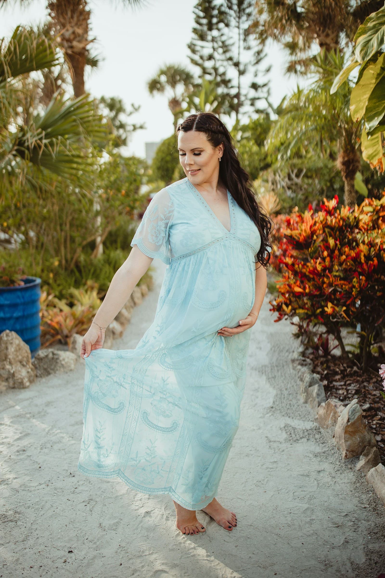 Pregnant woman in a flowing dress standing on a tropical garden path.