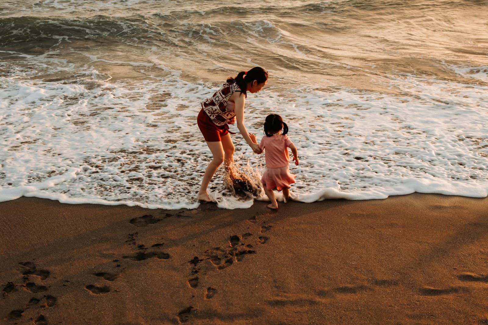 Parent and child playing at the edge of the ocean waves.