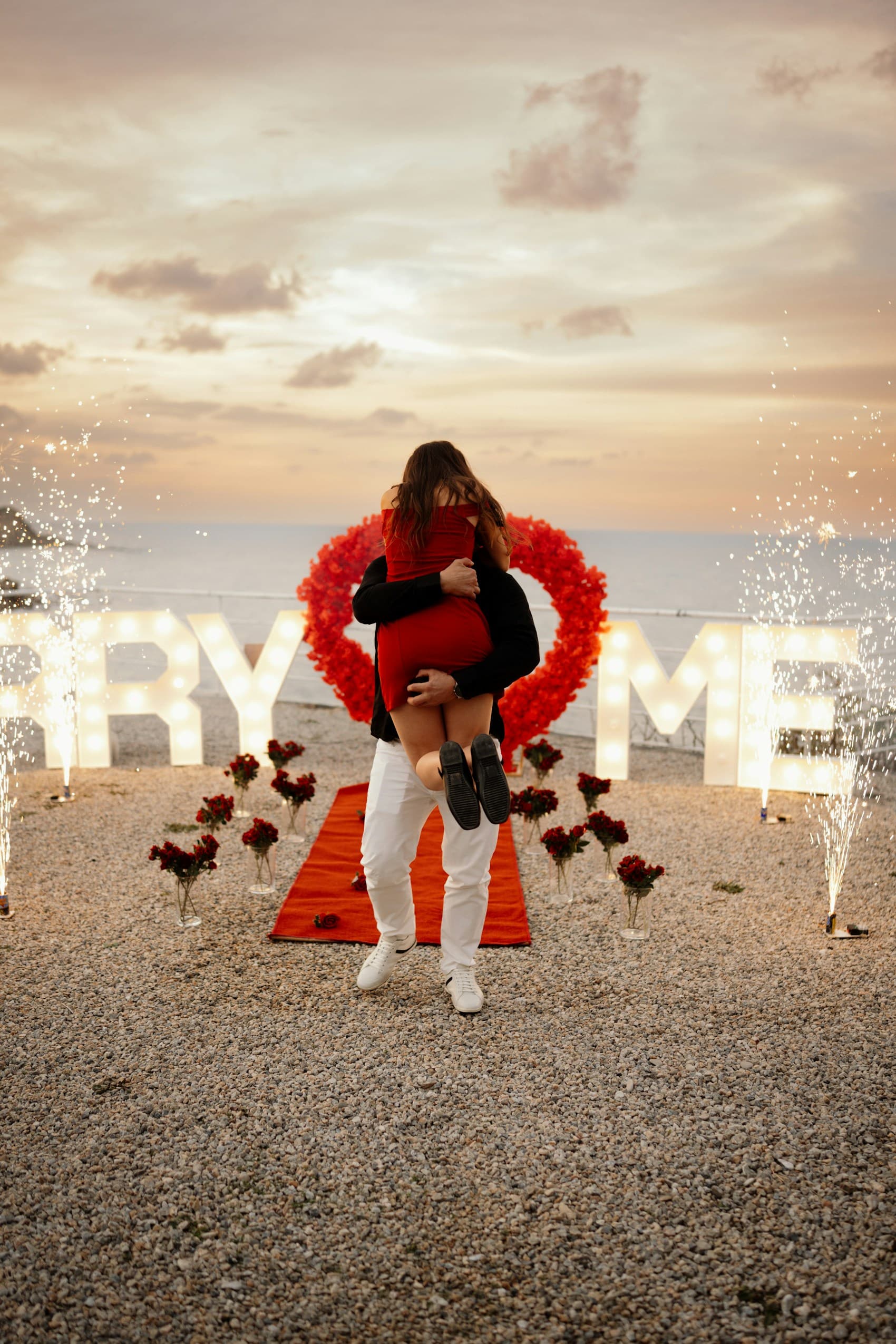 Couple embracing after a beach proposal with glowing marquee letters.