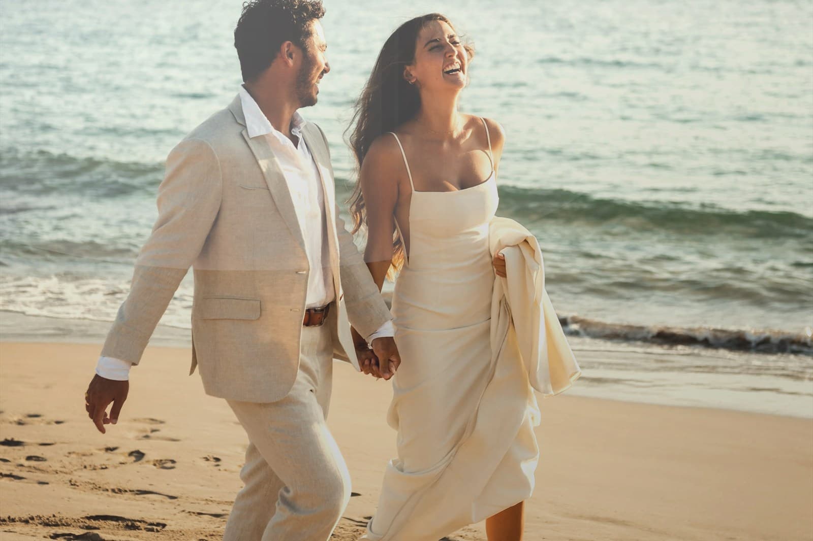 Hands holding baby shoes during a maternity beach session.