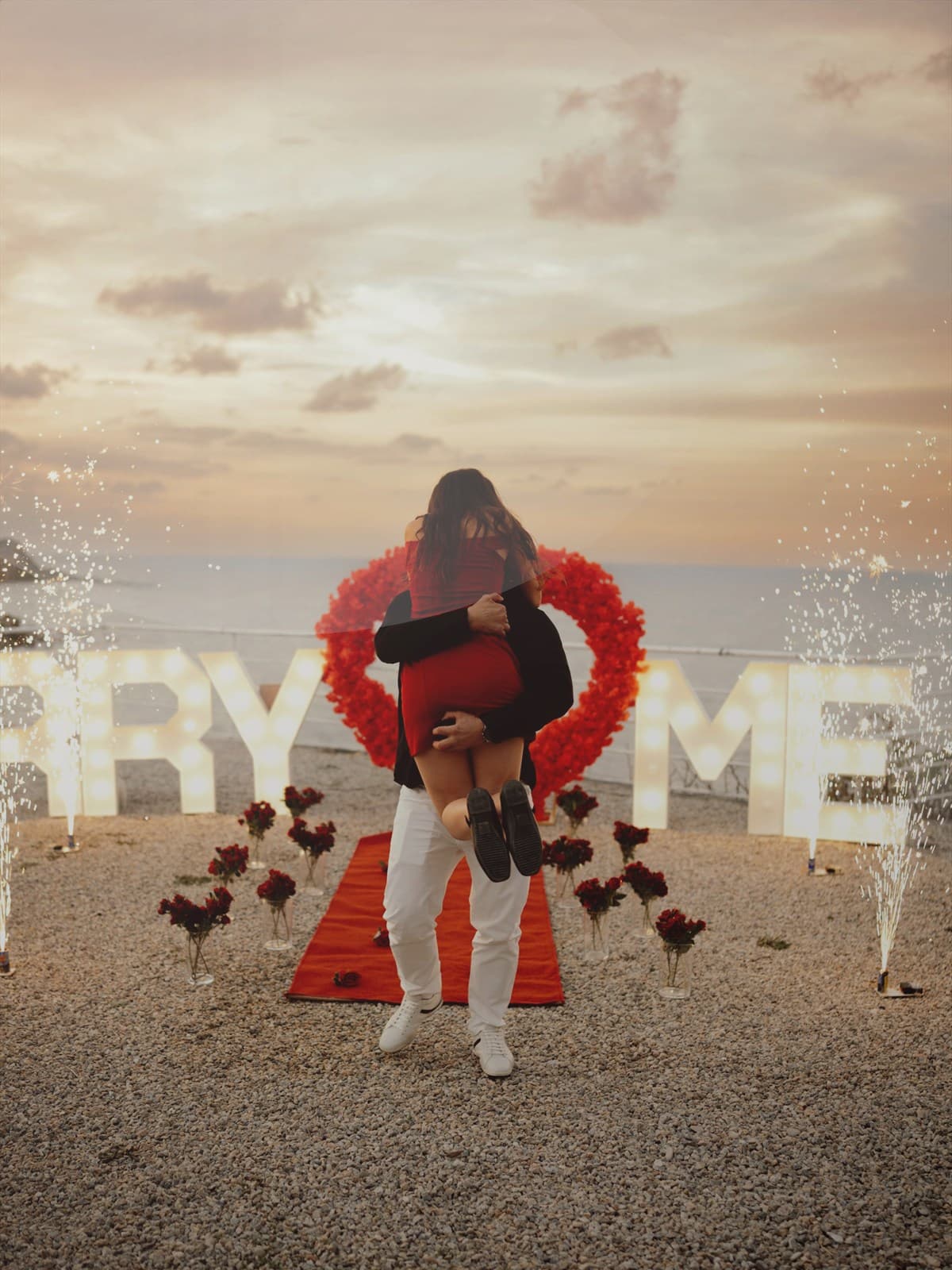 Bride and groom standing near the ocean on a rocky shoreline.